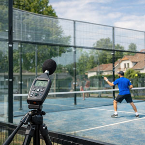 Sonomètre sur trépied mesurant le bruit d’un terrain de padel extérieur à proximité d’habitations